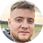 Мужчина с бородой в сером худи стоит на поле, создавая атмосферу спокойствия и уединения
